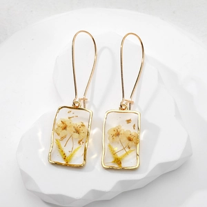 Detailed macro shot of handmade resin square earrings with yellow dried flowers and gold foil
