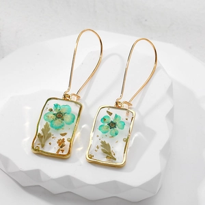 Macro detail of handmade resin square earrings with teal flowers and gold foil elements