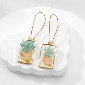 Macro detail of square gold earrings featuring dried flowers and gold foil in resin