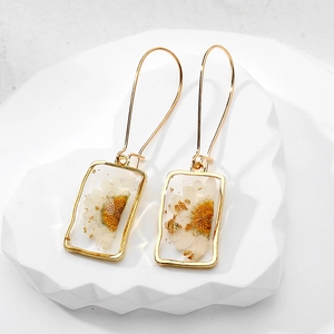 Macro shot of rectangular resin earrings with real dried daisies and gold foil flakes