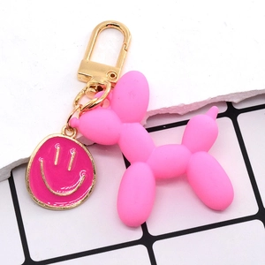 Dettaglio macro del ciondolo a cane palloncino rosa opaco e charm smiley su portachiavi dorato