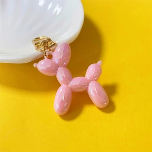 Detailed macro view of pink iridescent balloon dog keychain with gold metal clasp on yellow backdrop