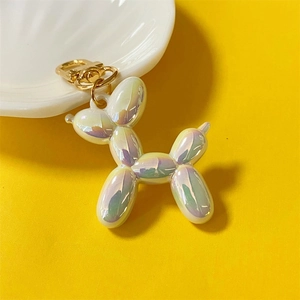 Detailed view of a pearlescent white balloon dog keychain with a gold metal clasp on yellow