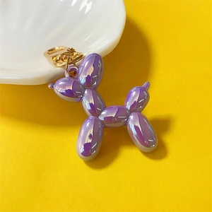 Iridescent purple metallic balloon dog keychain with golden clasp on yellow background