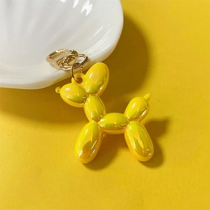 Glossy yellow metallic balloon dog keychain hanging on a white shell plate