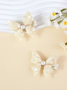 Détail de barrettes nœuds en dentelle crème avec perles sur un fond jaune chaleureux