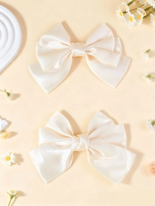 Close-up of a pair of elegant cream satin oversized bow hair clips with soft fabric texture