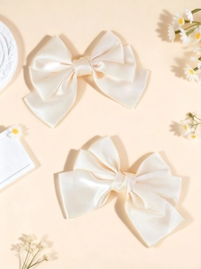 Close-up of two cream satin bow hair clips showing smooth texture and elegant ribbon layers