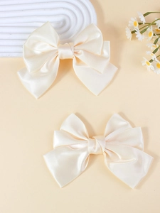 Close-up of two elegant cream satin oversized bow hair clips with layered fabric detail