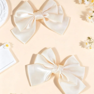 Elegant set of two creamy white oversized satin bow hair clips in a romantic floral setting