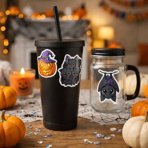 Close-up of Halloween stickers with pumpkin and bats on a black tumbler and mason jar