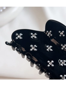 Close-up of black acetate hair claw clip with rhinestone and pearl flower details