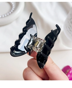Detail view of a glossy black butterfly hair claw clip featuring a sturdy metal spring
