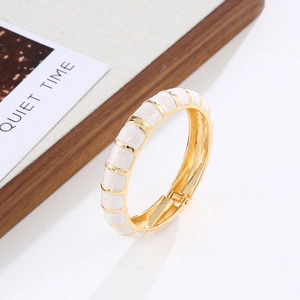Detail view of gold-plated hinged bangle with white enamel inlay and bamboo-like texture