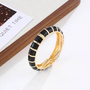 Detail of bohemian gold metal bangle with black enamel segments and hinged clasp closure