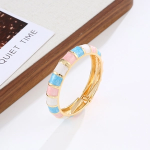 Detail of bohemian gold hinge bangle with colorful enamel inlays on a stylish wooden tray