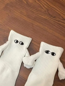 Détail de chaussettes blanches aimantées se tenant par la main sur fond de bois