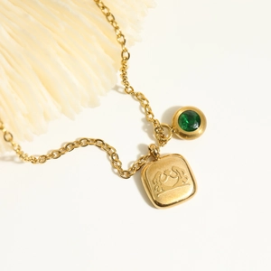 Close-up of golden stainless steel necklace featuring green gemstone and embossed pendant
