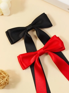Detail of red and black satin bow hair clips with long tassels on a textured surface