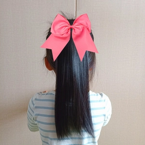 Bright pink oversized satin bow hair clip accessory worn on a black ponytail style