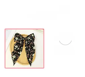 Detailed view of the black floral bow hair clip with long ribbons on a wooden tray