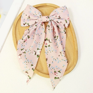 Elegant pink floral bow hair clip with long ribbons on a rustic wooden tray decor