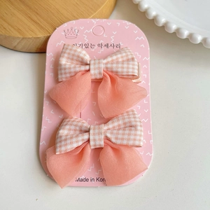 Détail des barrettes à nœud en tissu à carreaux orange et tulle sur carte rose
