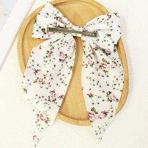 Floral print chiffon bow hair clip with pink rose patterns on a wooden tray