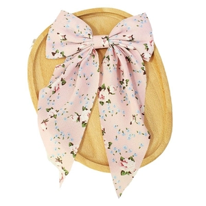Pink floral bow hair clip with rose patterns and long flowing ribbons on wooden tray