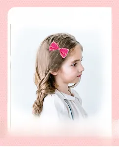 Detail view of a rose red ribbon bow hair clip with pearl trim worn by a child model