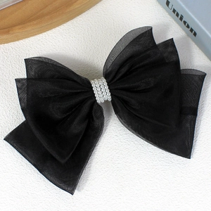 Elegant black multi-layer mesh bow hair clip with white pearl center on white surface
