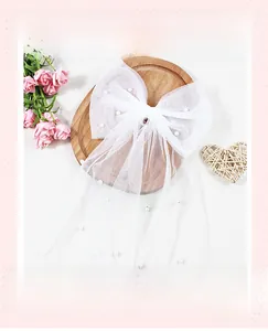 Détail de la pince à cheveux mariée en tulle blanc avec perles sur plateau bois