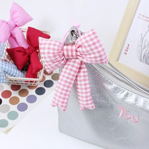 Pink and white checkered bow charm on a silver bag with a soft aesthetic style