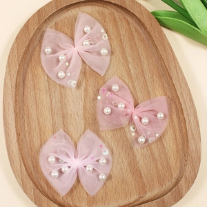Three pink mesh bow hair accessories with pearls and sequins on an oval wooden tray
