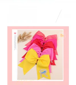 Détail de la pince à cheveux nœud jaune avec broderie lettre R et motif plume