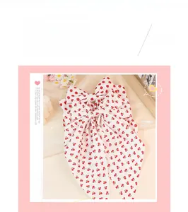 Detail view of white chiffon bow hair clip with red cherry prints and long ribbons
