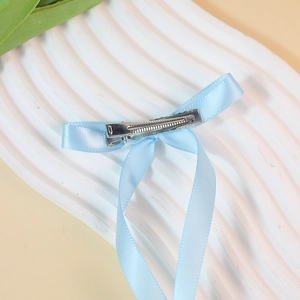 Light blue satin ribbon bow hair clip with long streamers on elegant white texture
