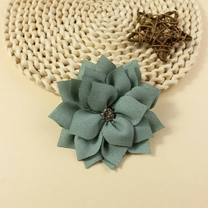 Detail of dark green layered chiffon flower with a crystal center on a beige mat