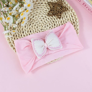 Detail of pink cotton baby headband featuring a white bow with scalloped embroidery