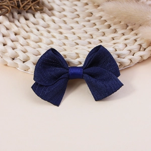 Detail of a navy blue ribbon bow hair clip with textured fabric on a rustic straw mat