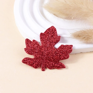 Detail of red glitter maple leaf hair clip on a minimalist warm beige background