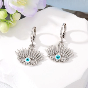 Boucles d'oreilles œil maléfique argentées avec cristaux et détails bleus sur un socle