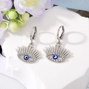 Détail de boucles d'oreilles œil de démon avec cils et strass sur socle en pierre