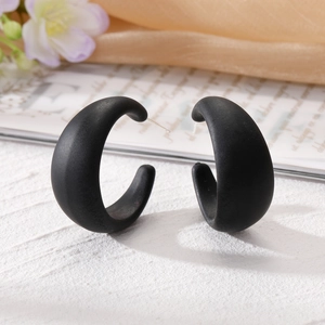 Vue macro de boucles d'oreilles créoles géométriques noires mates sur une surface texturée