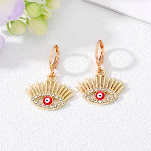 Gros plan de boucles d'oreilles Evil Eye dorées avec pupilles rouges et strass blancs