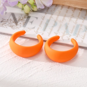 Gros plan sur des créoles orange mat en forme de C sur une surface texturée élégante