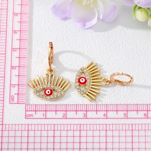 Gros plan de boucles d'oreilles œil porte-bonheur dorées avec émail rouge et cristaux