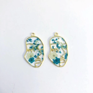 Detail of face-shaped gold frame earrings with blue and white preserved dried flowers