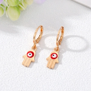 Golden Hamsa Hand earrings with Evil Eye charms and hoop closure on white textured background