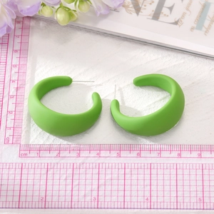 Vue détaillée des boucles d'oreilles créoles C en résine vert mat sur fond blanc